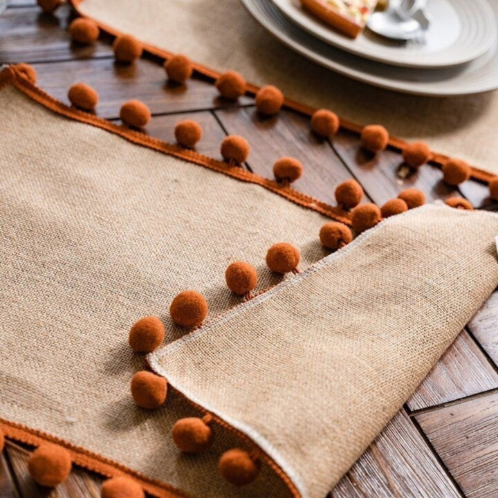 Jute-Tischläufer mit orangefarbenen Pompons