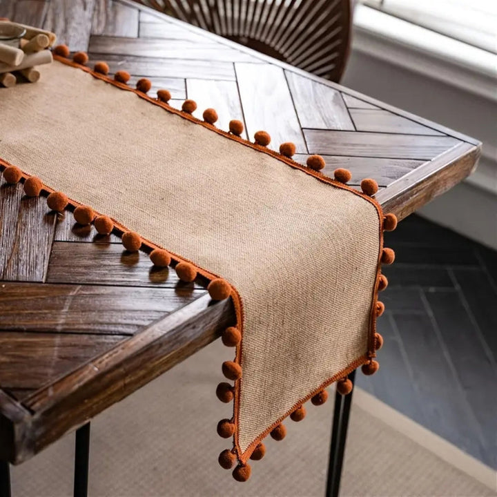 Jute-Tischläufer mit orangefarbenen Pompons